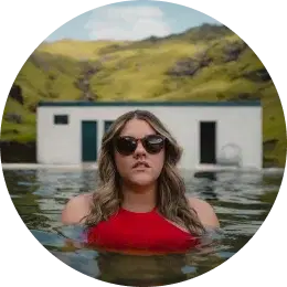 Femme en maillot de bain rouge et lunettes de soleil profitant d'une piscine d'eau chaude naturelle en Islande.