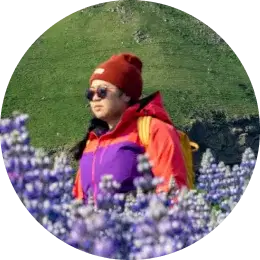 Voyageur portant un bonnet rouge et une veste colorée marchant à travers un champ de lupins violets en Islande.