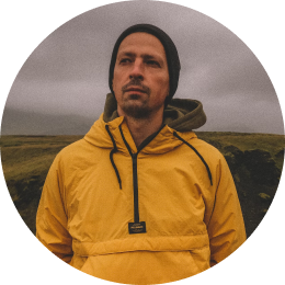 Voyageur portant une veste de pluie jaune, debout dans le paysage sombre et couvert de l'Islande.