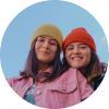 Deux jeunes femmes avec des chapeaux colorés souriant en plein air.