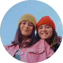 Deux jeunes femmes avec des chapeaux colorés souriant en plein air.