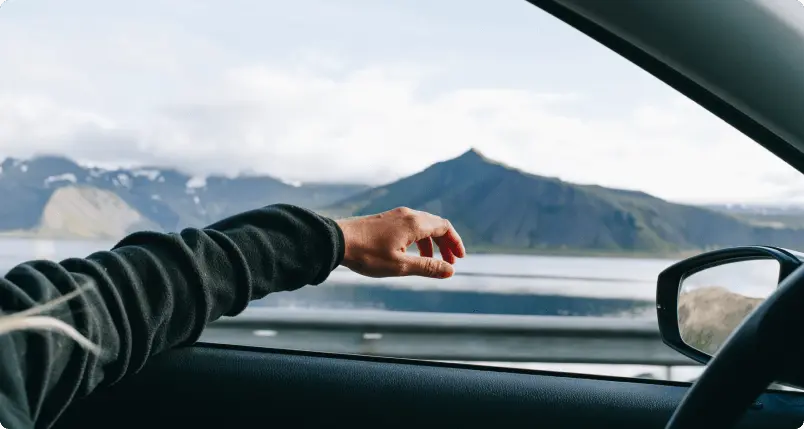 Une main sortant d'une fenêtre de voiture en roulant à travers les paysages pittoresques de l'Islande, représentant l'assistance routière fiable de Cars Iceland pour un voyage sans souci.