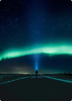 Silhouette d’une personne avec une lampe de poche sous les aurores boréales en Islande, illuminant le ciel nocturne rempli d’étoiles.