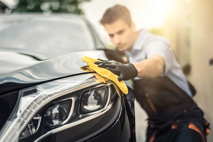 Un homme nettoie et polit le phare d'une voiture noire avec un chiffon jaune, concentré sur son travail.