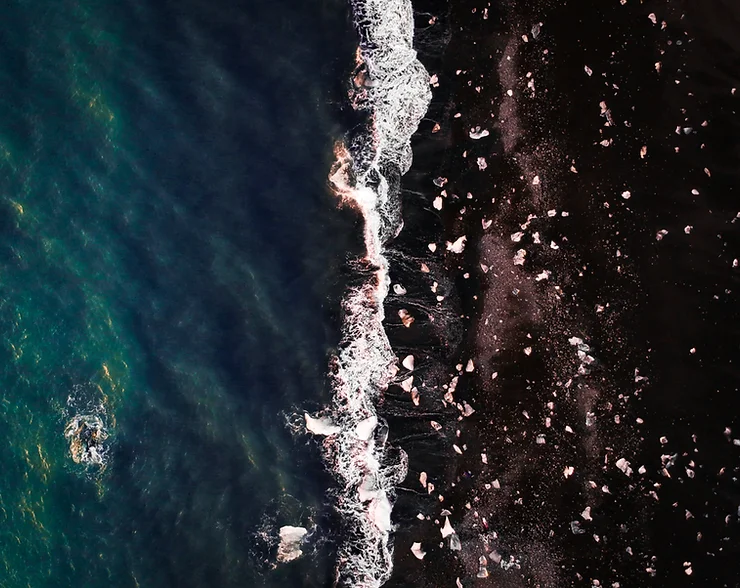 Vue aérienne de la plage de diamants en Islande, avec vagues blanches et blocs de glace sur le sable noir.