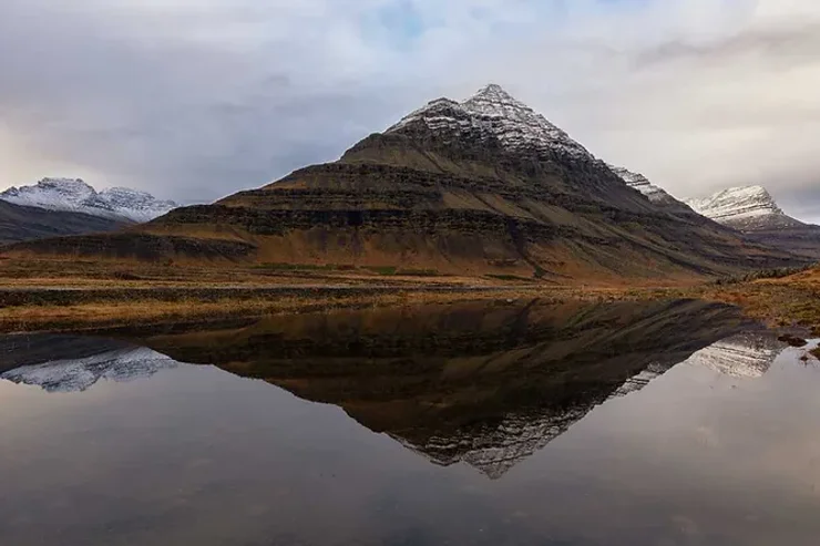 Paysage montagneux enneigé parfaitement reflété dans les eaux calmes d’un lac.