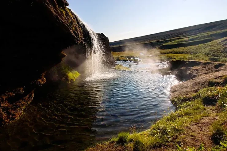 Petite cascade chaude naturelle entourée de verdure dans un paysage isolé en Islande.