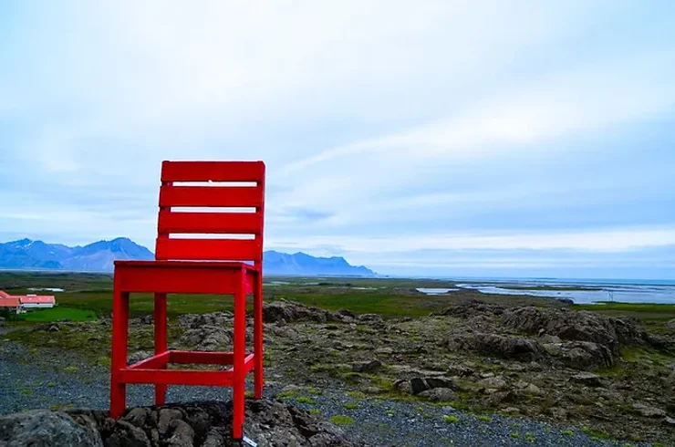 Une grande chaise rouge posée sur un terrain rocheux avec vue panoramique sur un paysage islandais et l’océan.