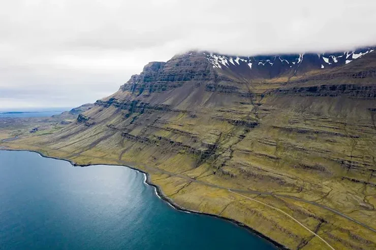 Vue aérienne d’une montagne islandaise imposante avec des pentes verdoyantes se jetant dans l’océan.