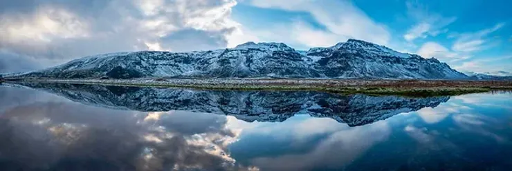 Paysage montagneux enneigé parfaitement reflété dans les eaux calmes d’un lac.