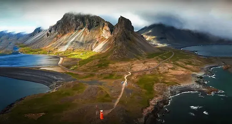 Vue aérienne spectaculaire d'une péninsule islandaise avec montagnes escarpées, plages noires et un phare rouge.