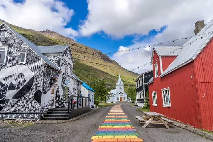 Rue colorée dans un village islandais pittoresque, bordée de maisons traditionnelles et menant à une église blanche.