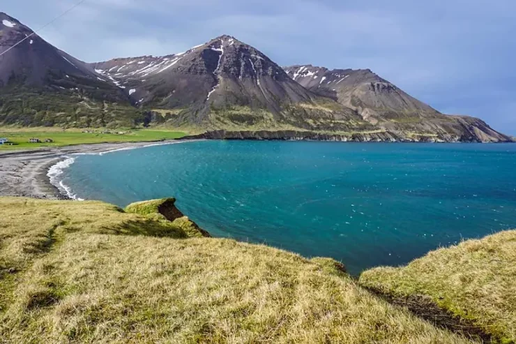 Baie islandaise avec une eau turquoise et des montagnes impressionnantes en arrière-plan.