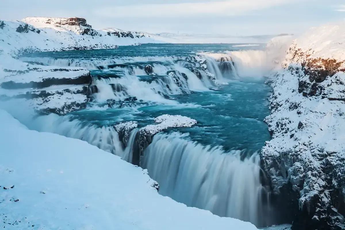 La cascade Gullfoss recouverte de neige avec des eaux turquoise qui s'écoulent entre les rochers.