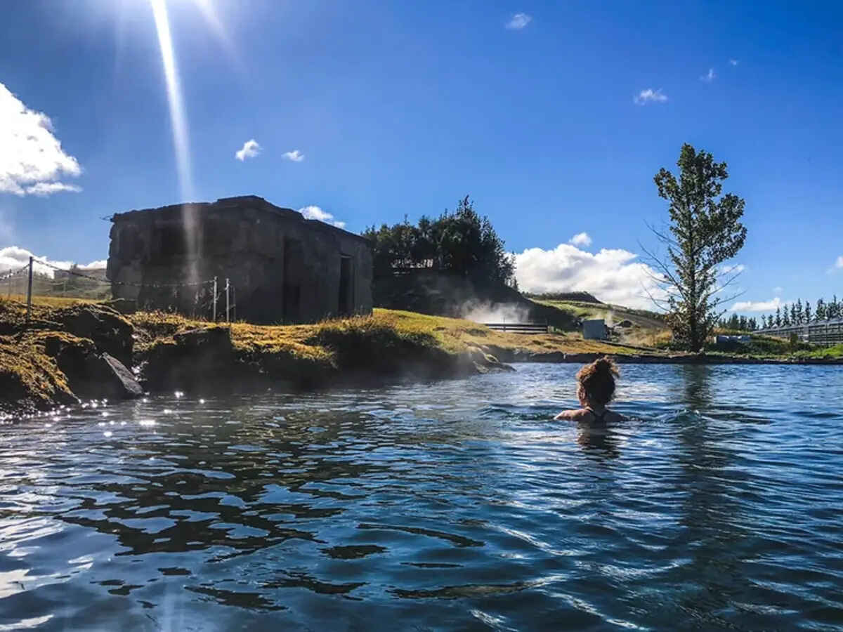 Personne se relaxant dans la Secret Lagoon entourée de paysages naturels islandais.