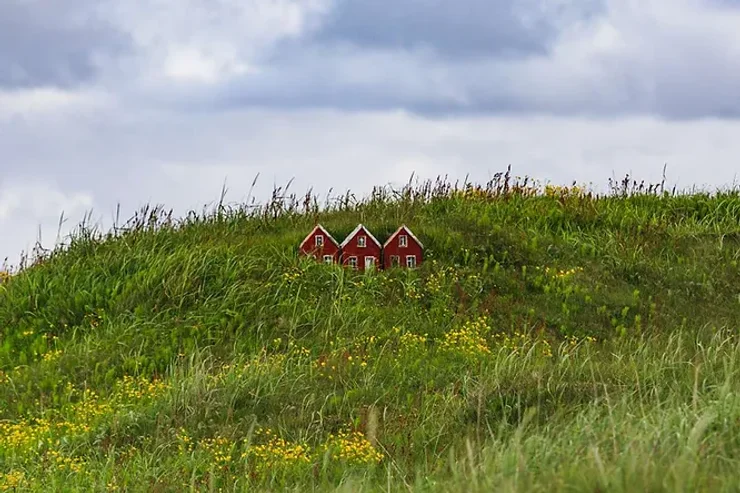 Un groupe de petites maisons rouges d'elfes nichées sur une colline verdoyante et entourées de fleurs jaunes, sous un ciel nuageux.