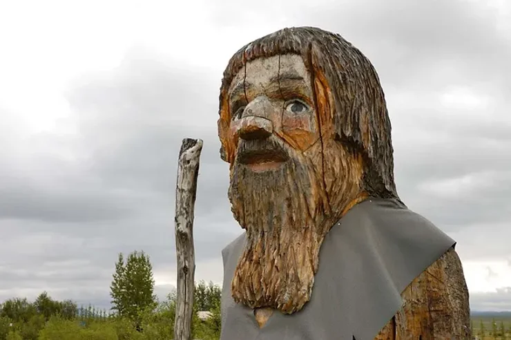 Grande statue sculptée en bois représentant un troll islandais avec une apparence rustique et réaliste, dans un paysage naturel.