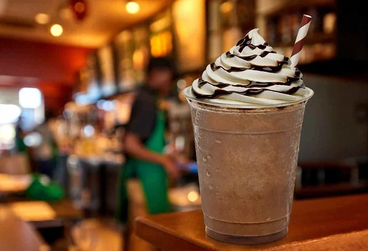 Un frappuccino avec crème fouettée et sauce au chocolat, posé sur une table en bois dans un café chaleureux.