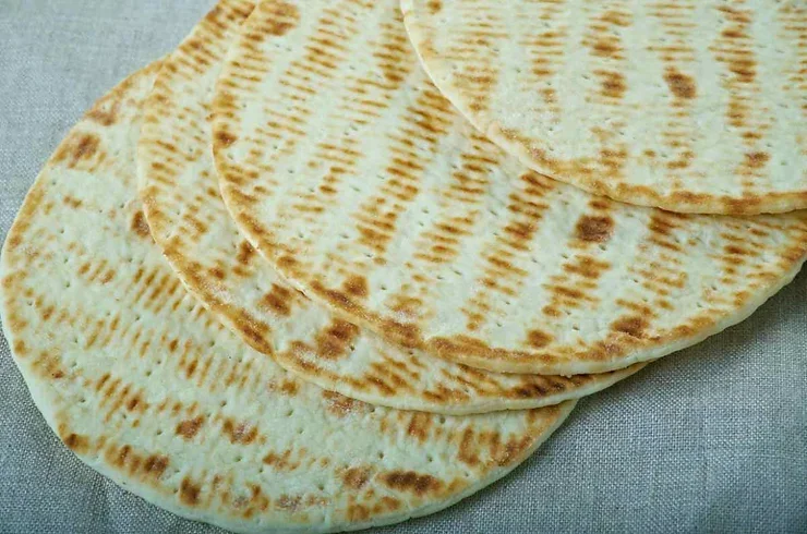 Un déjeuner typiquement islandais Gros plan sur plusieurs pains plats islandais traditionnels disposés sur un tissu beige, montrant leur texture dorée et légèrement grillée.