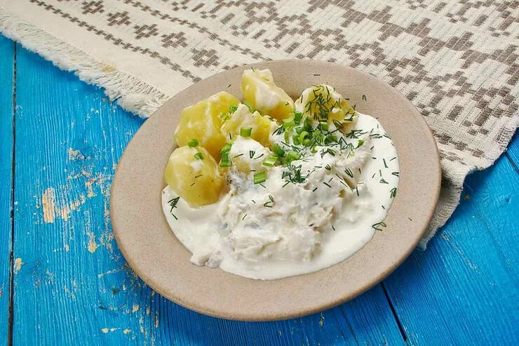 Plokkfiskur: ragoût de poisson traditionnel islandais Un plat de ragoût de poisson islandais, accompagné de pommes de terre et d'une sauce crémeuse, présenté sur une assiette beige.