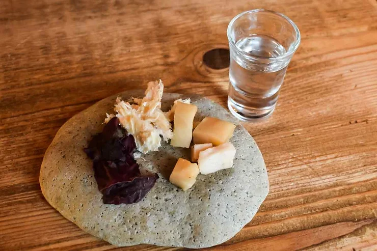 Hakarl - Requin fermenté Assiette traditionnelle islandaise avec du requin fermenté, des morceaux de poisson séché, des cubes de fromage et une feuille d'algue, accompagnée d'un verre d'alcool clair.