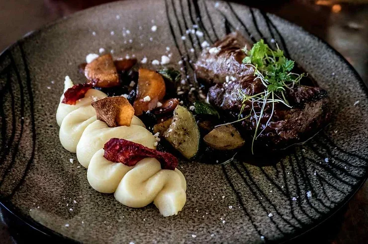Viande de macareux Assiette élégante d'un plat islandais raffiné avec un morceau de viande tendre accompagné de purée de pommes de terre crémeuse, garnie de chips croustillantes et de légumes colorés rôtis, décorée de fines herbes.