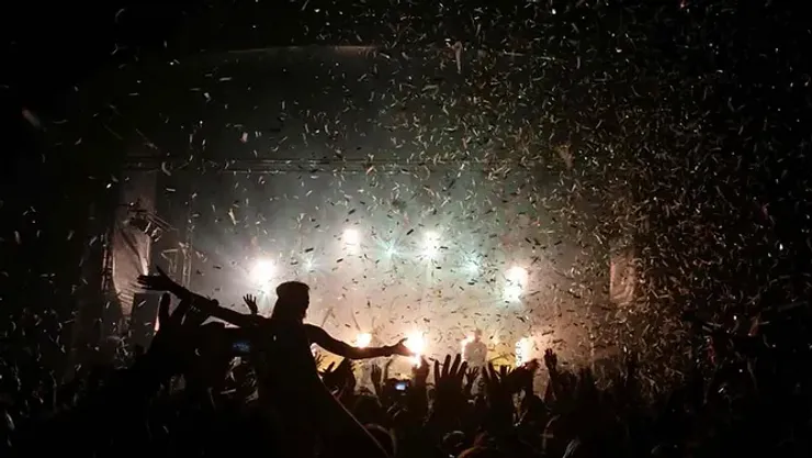Une foule en liesse dans un concert, sous une pluie de confettis, illuminée par des projecteurs chaleureux.