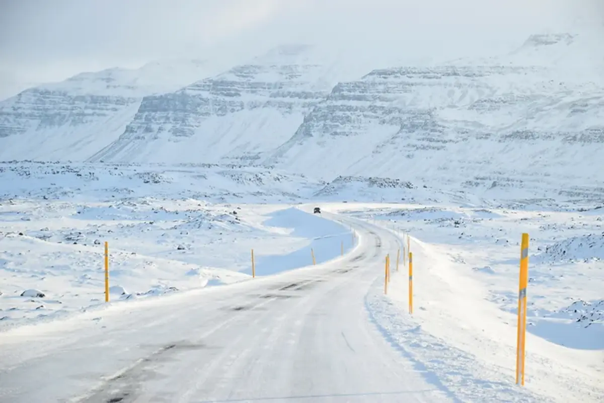 Une route recouverte de neige menant à des montagnes majestueuses sous un ciel rose pastel.