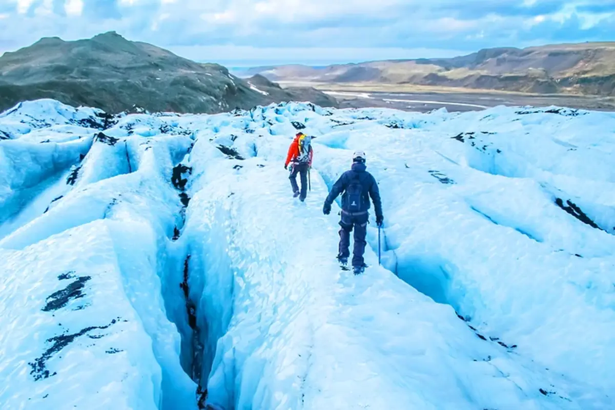 Deux randonneurs explorant un glacier spectaculaire en Islande, entourés de crevasses de glace bleue éclatante.