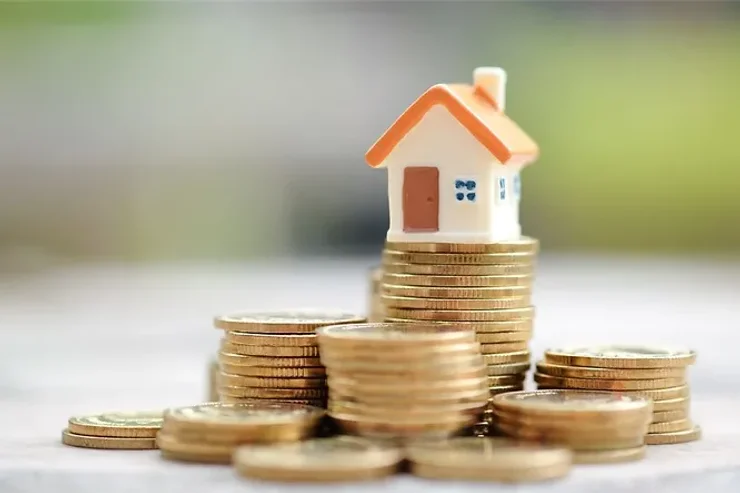 Maison miniature posée sur des piles de pièces dorées, représentant l'investissement immobilier en Islande.