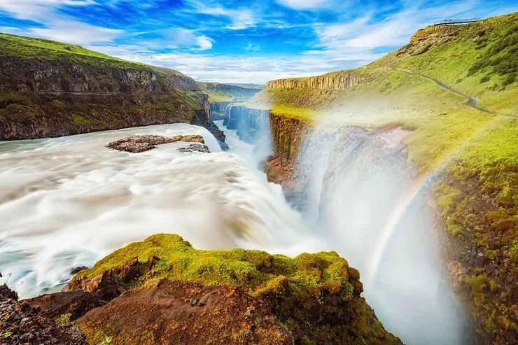 La cascade impressionnante de Gullfoss, illumin&eacute;e par un arc-en-ciel sous un ciel bleu &eacute;tincelant, au c&oelig;ur du Cercle d&rsquo;Or.