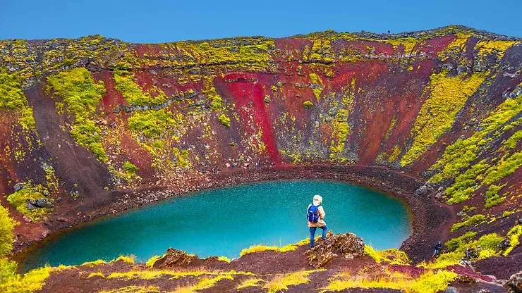 Vue color&eacute;e du crat&egrave;re Kerid en Islande avec son lac bleu entour&eacute; de collines aux teintes rouges et vertes.