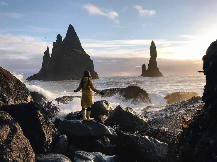 Vue captivante des formations rocheuses de Reynisdrangar &eacute;mergeant de l'oc&eacute;an, entour&eacute;es par les vagues tumultueuses des plages de sable noir islandaises.