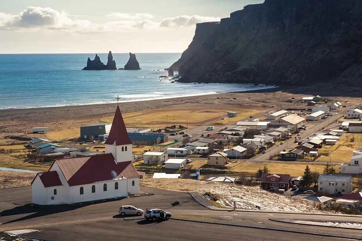 Le village de V&iacute;k, nich&eacute; entre falaises et mer, avec sa c&eacute;l&egrave;bre &eacute;glise au toit rouge entour&eacute;e de paysages verdoyants.