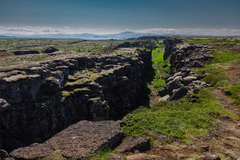 Fissure des plaques tectoniques à Þingvellir, en Islande, avec des roches verdoyantes et un ciel dégagé.