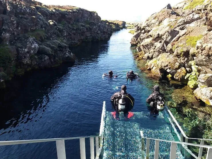 Des plongeurs en combinaison étanche explorent la faille de Silfra, un site unique entre les plaques tectoniques eurasienne et nord-américaine, dans des eaux cristallines d'Islande.