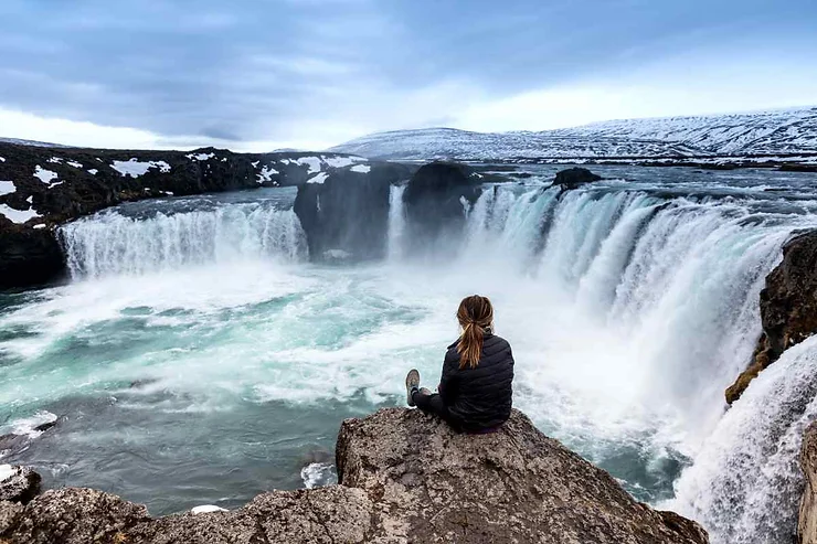  Vue panoramique d'une cascade majestueuse entourée de neige, avec une personne assise contemplant le paysage.