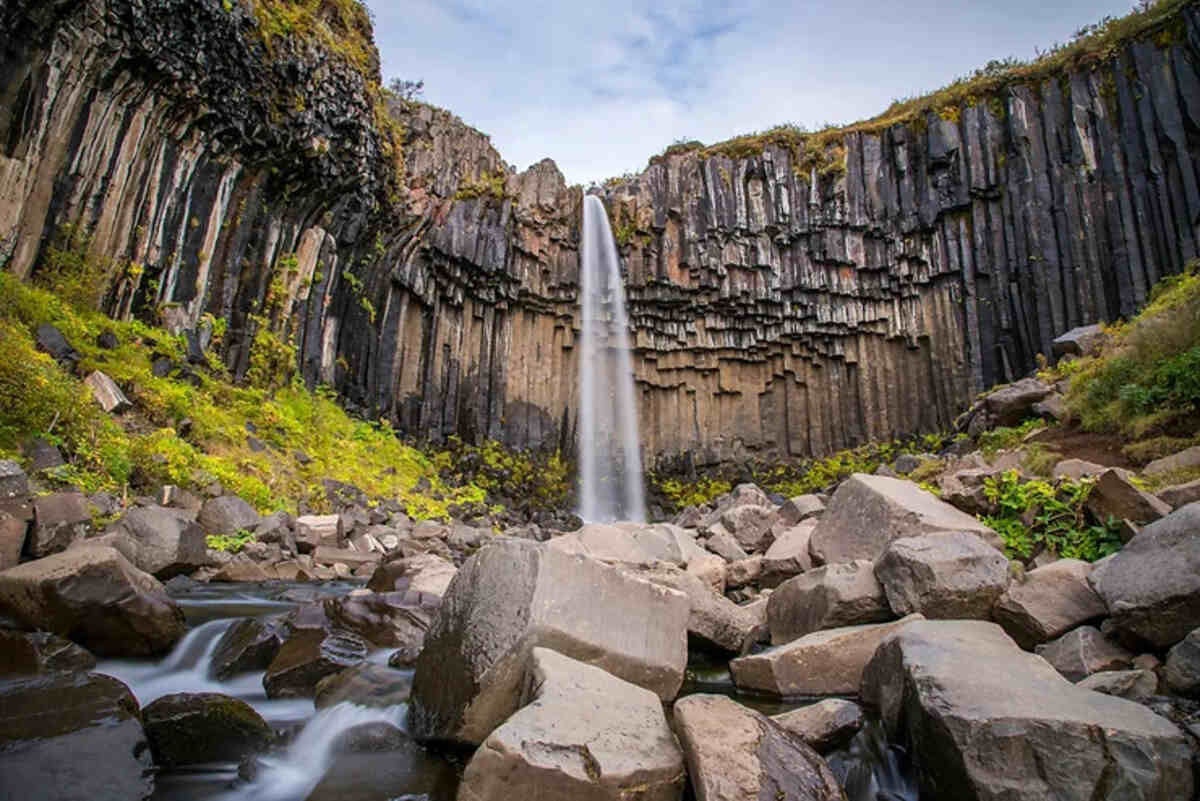 Une vue spectaculaire de la cascade Svartifoss, entourée de colonnes de basalte noir emblématiques, au cœur du parc national de Skaftafell en Islande.