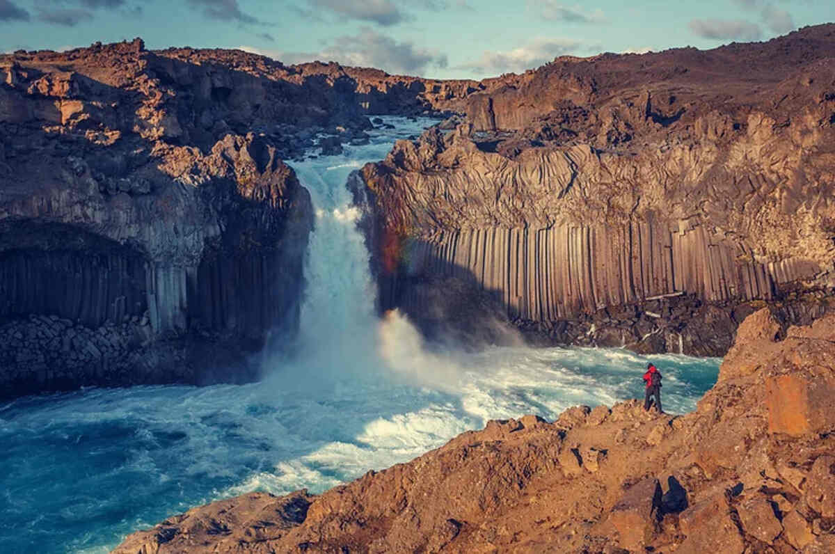 La cascade Aldeyjarfoss au nord de l'Islande, plongeant dans une piscine d'eau turquoise, entourée par des formations géologiques uniques de colonnes de basalte.