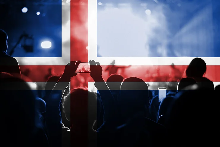 Une foule lors d'un événement avec le drapeau islandais superposé en transparence. Quelques personnes prennent des photos avec leur téléphone.