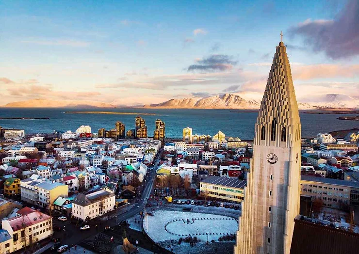 Vue panoramique de Reykjav&iacute;k, avec l'&eacute;glise Hallgr&iacute;mskirkja au premier plan et les montagnes enneig&eacute;es &agrave; l'arri&egrave;re-plan.