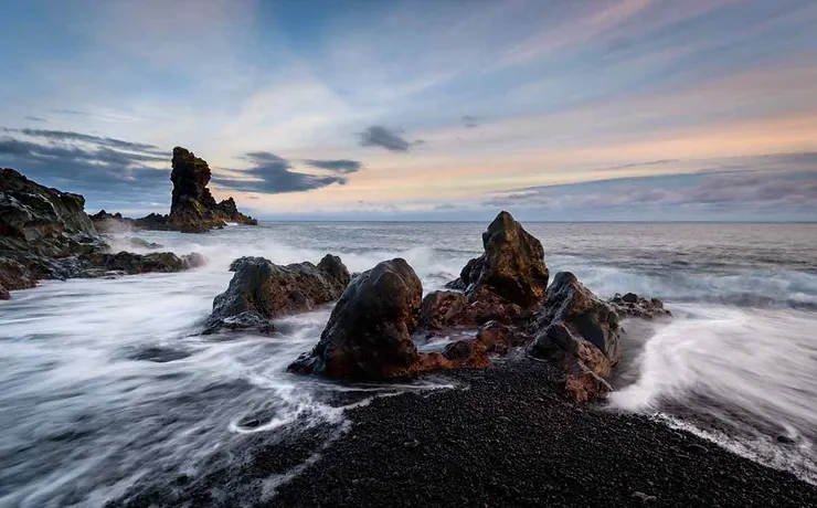 Une c&ocirc;te rocheuse en Islande avec des eaux en mouvement et un ciel couchant.