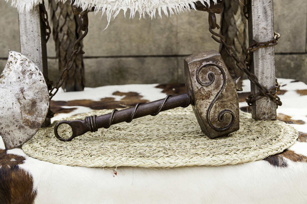 Une reproduction de Mjölnir, le marteau de Thor, en métal avec des détails incrustés, repose sur une base en paille à côté d'autres éléments décoratifs de style nordique.