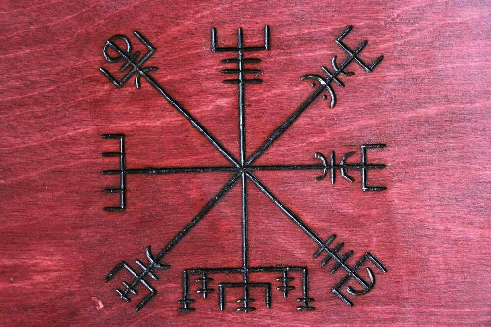 Représentation du symbole Aegishjalmur, également connu sous le nom de « casque de la terreur », gravé en noir sur une surface en bois rouge.