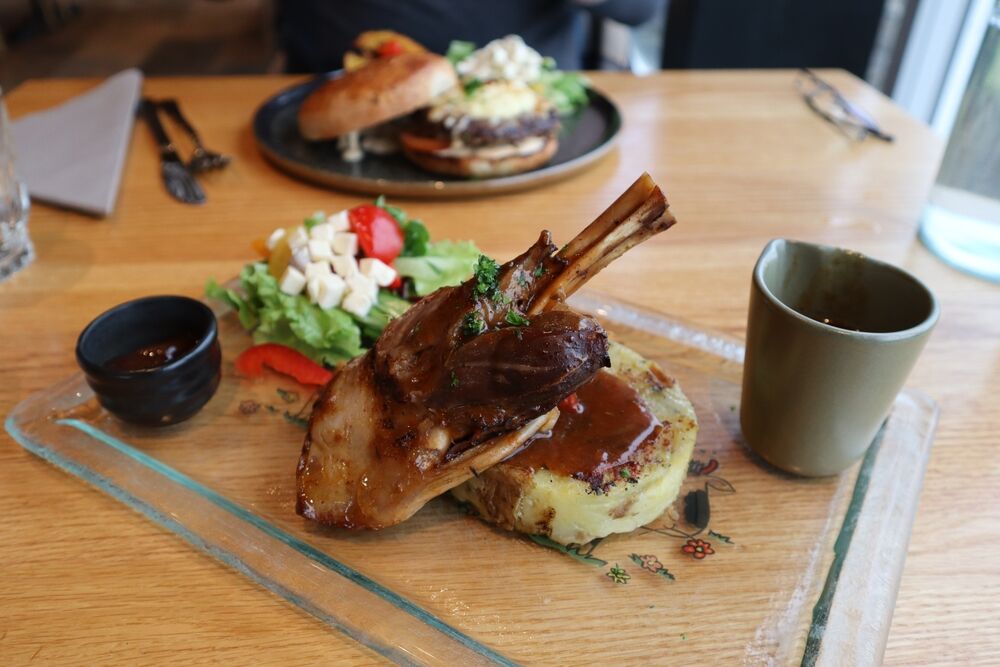 Un plat d'agneau r&ocirc;ti servi sur un plateau en verre, accompagn&eacute; de pur&eacute;e de pommes de terre et de sauce, d'une salade fra&icirc;che et d'une tasse de sauce fumante.