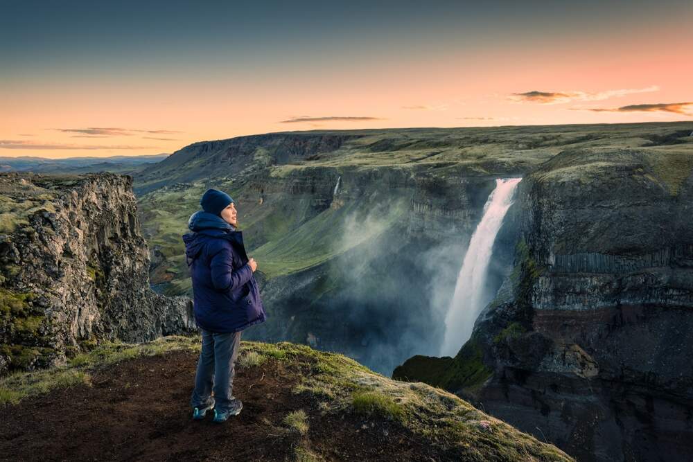 Un randonneur contemplant la cascade Haifoss au lever du jour, entouré d'un paysage volcanique.