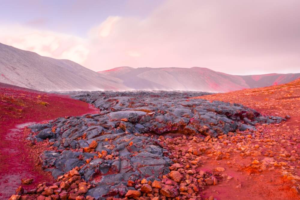 Paysage volcanique islandais avec des coulées de lave solidifiées d'un rouge profond sous un ciel rose.