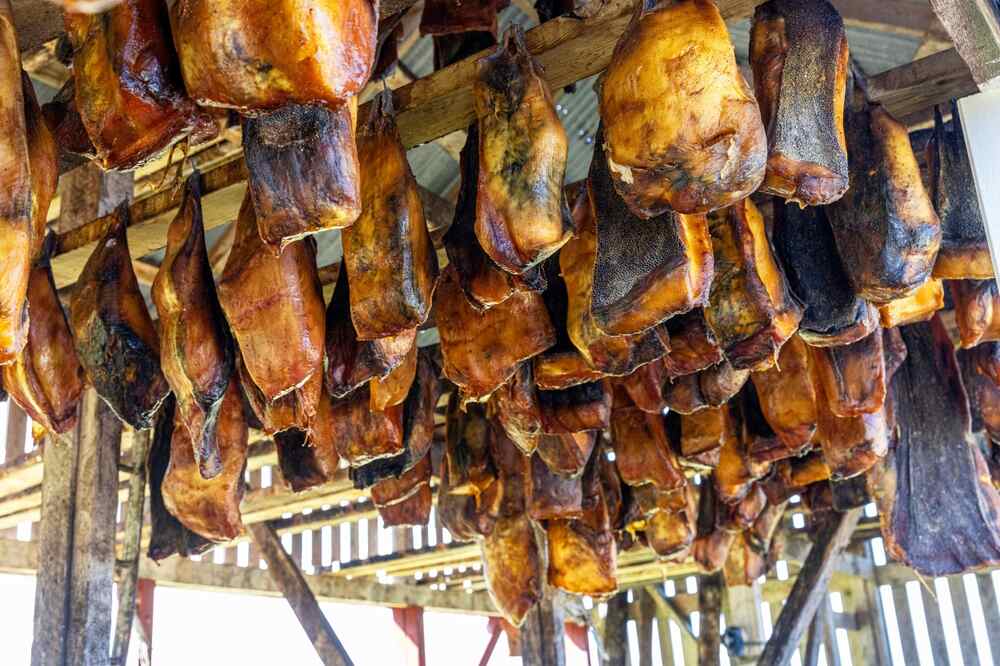 Des morceaux de viande de requin suspendus dans un séchoir en bois, montrant la texture dorée et séchée des morceaux fermentés.