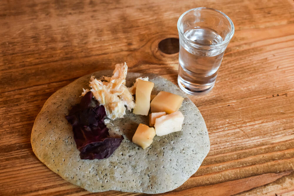 Un plat traditionnel islandais composé de morceaux de requin fermenté, d'algues séchées et de fromage disposés sur une galette avec un verre d'eau-de-vie claire.