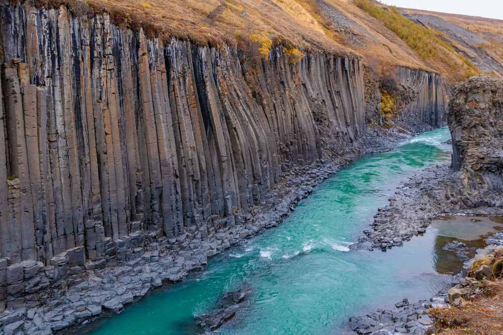Vue sur le canyon de Stuðlagil avec ses colonnes basaltiques imposantes bordant une rivière turquoise, créant un paysage à couper le souffle.
